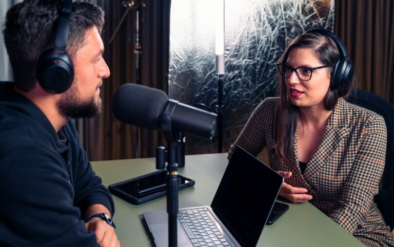 a man and a woman wearing headphones and looking at a laptop